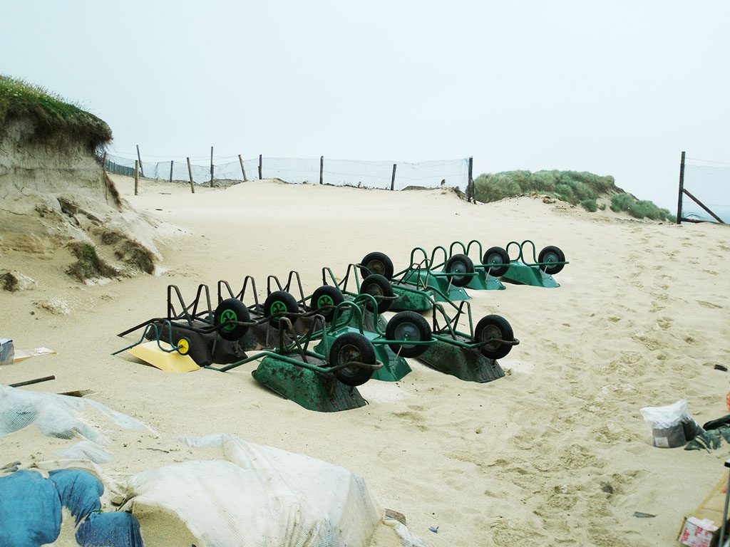 Wheelbarrows lying upside down in a row on a sandy beach.